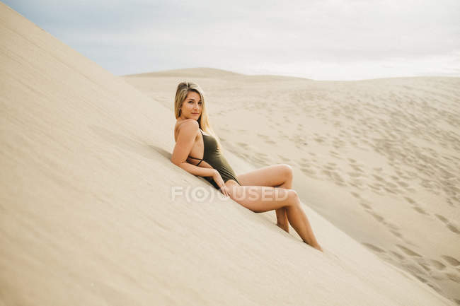Portrait of sensual young woman in black swimsuit lying on sand dune — Stock Photo