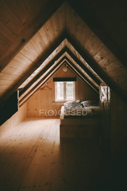Acogedor pequeño desván de madera habitación interior con cama y ventana PROPIEDAD - foto de stock