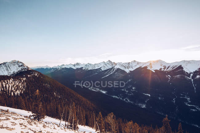 Bosque de invierno en colinas nevadas en el fondo con cielo nublado y sol? con pintorescas montañas con ríos de tierras altas - foto de stock