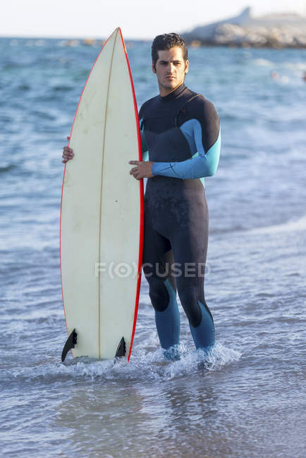 Портрет красивого мужчины, держащего доску для сёрфинга на пляже — стоковое фото