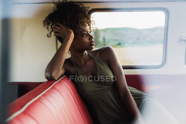 Attraktive Afroamerikanerin sitzt auf der bequemen Rückbank eines Oldtimers und schaut weg, während sie auf dem Land unterwegs ist — Stockfoto