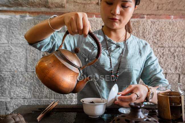 Mujer asiática joven vertiendo agua de la olla mientras hace el té en la ceremonia tradicional - foto de stock