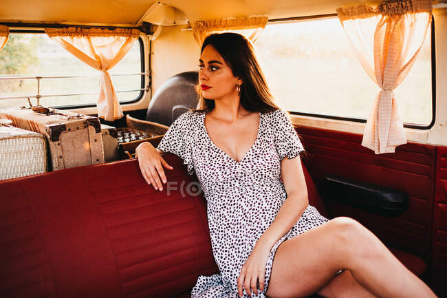 Joven mujer atractiva sentada en furgoneta vintage y mirando hacia otro lado - foto de stock