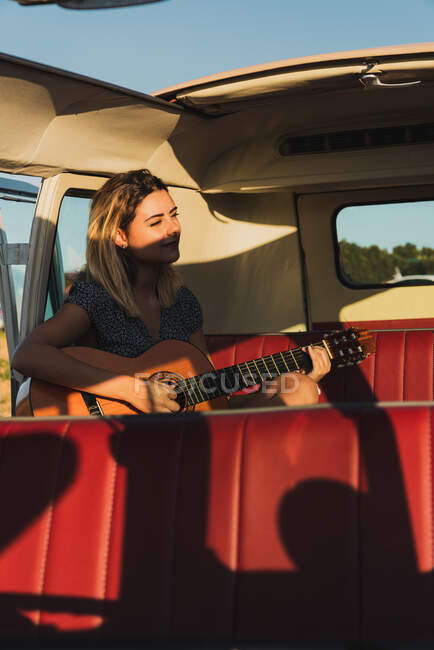 Woman playing acoustic guitar while sitting inside retro van during trip — Stock Photo