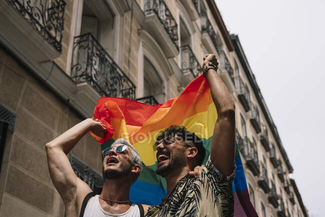 Pareja de chicos con bandera de orgullo gay en la calle de Madrid - foto de stock