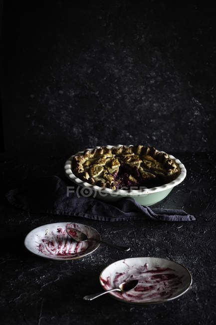 Tarte aux cerises appétissante dans un plat avec deux soucoupes vides sur fond sombre — Photo de stock