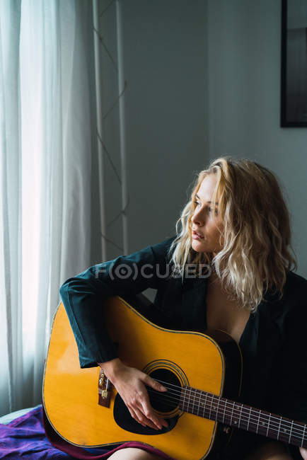 Rubia joven tocando la guitarra en la cama en casa - foto de stock