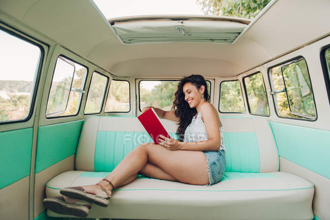 Mulher sentada dentro caravana retro e livro de leitura — Fotografia de Stock