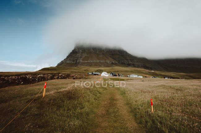 Perspectiva de la pequeña senda hacia el asentamiento entre colinas en las Islas Feroe - foto de stock