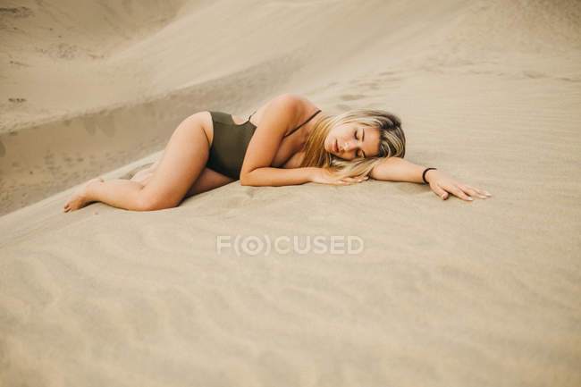 Sensual joven con los ojos cerrados en traje de baño acostado en la arena - foto de stock