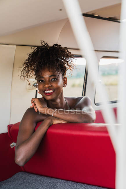 Attractive African-American female sitting on comfortable back seat of vintage van and looking away while traveling in countryside — Stock Photo