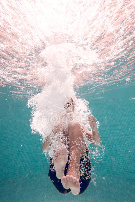 Menino irreconhecível em troncos de natação mergulhando na água da piscina azul transparente — Fotografia de Stock