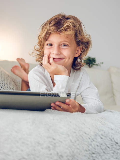 Fröhlicher Junge mit digitalem Tablet auf Couch liegend — Stockfoto