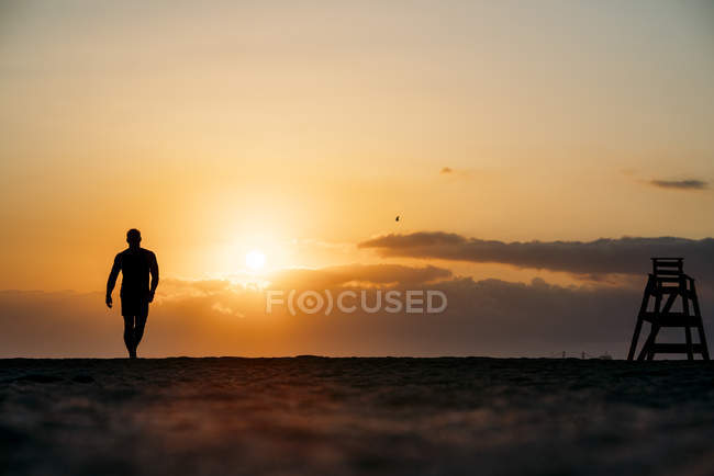 Silueta del hombre caminando en la playa - foto de stock