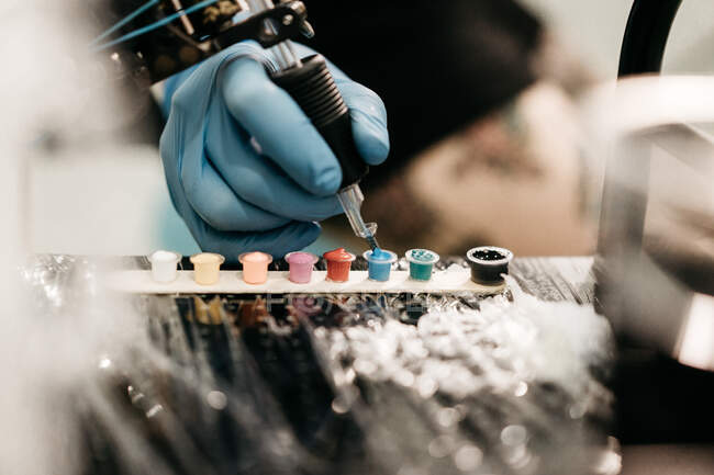 Crop mano in guanto di lattice prendendo inchiostro blu mentre fa il tatuaggio in studio — Foto stock