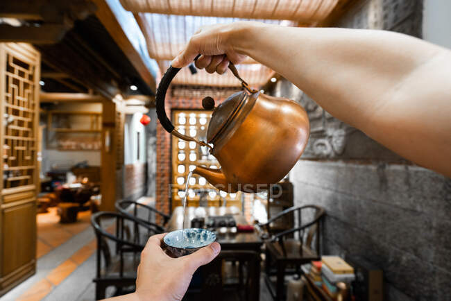 Cortar la mano vertiendo agua de la tetera de cobre a la taza durante la ceremonia del té oriental - foto de stock
