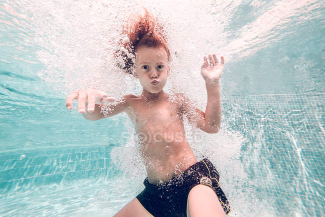Capretto dai capelli rossi che si tuffa in acqua sullo sfondo di acqua trasparente — Foto stock