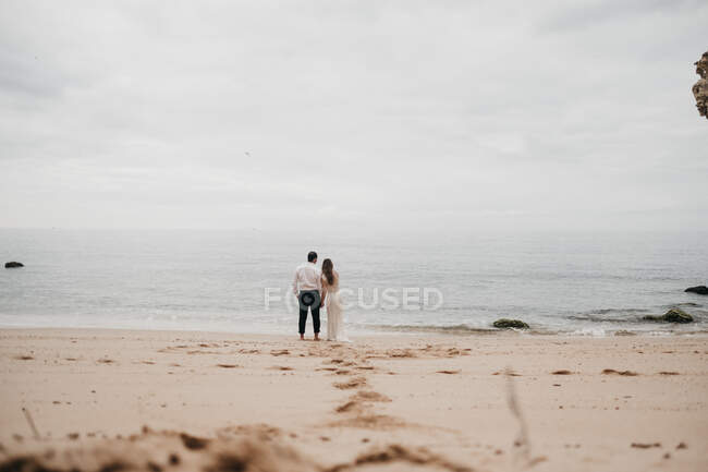 Newlyweds standing on sand of ocean — Stock Photo