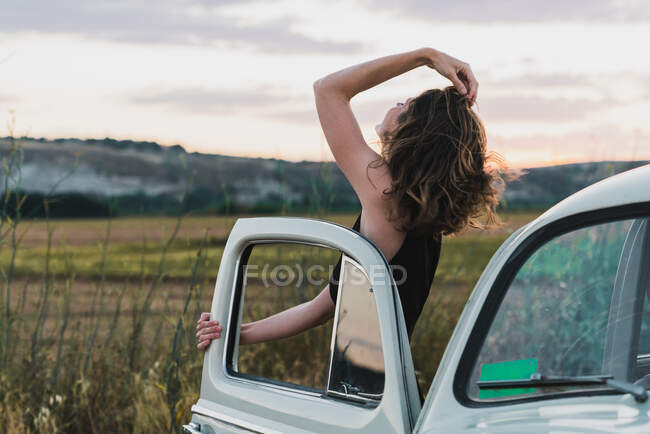 Mujer apoyada en un coche de época en el campo - foto de stock