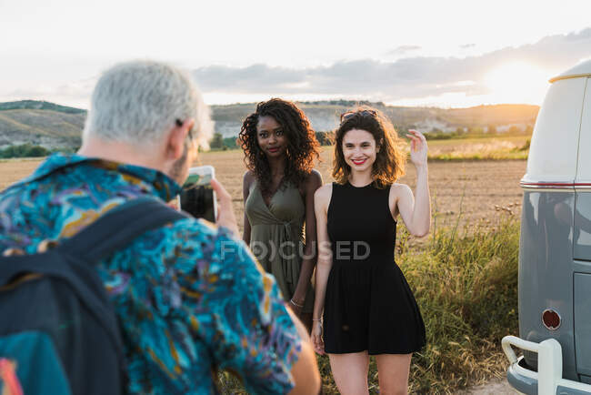 Cara irreconhecível usando smartphone para tirar fotos de duas mulheres adoráveis enquanto passar tempo na natureza juntos — Fotografia de Stock