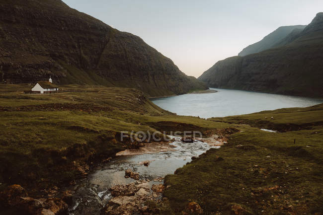 Solitaria casita en verdes montañas en el lago en nublado, Islas Feroe - foto de stock