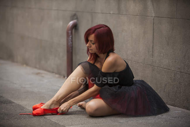 Bailarina de cabeza roja con tutú negro aplastando consejos de ballet rojo en la calle - foto de stock