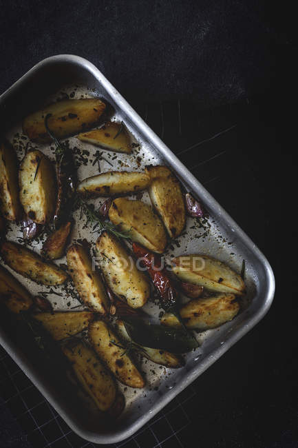 Gebratene goldene knusprige Kartoffelkeile in Backform auf schwarzer Oberfläche — Stockfoto