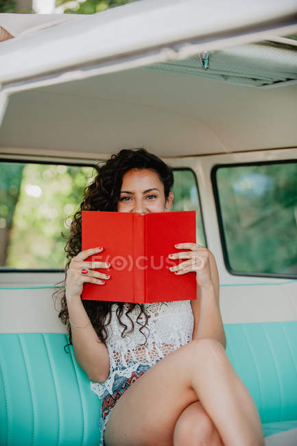 Retrato de la mujer sentada dentro de la caravana retro y libro de celebración - foto de stock