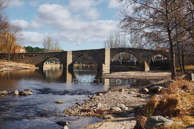 Alte schöne Brücke mit Bögen über ruhigen, flachen Fluss vor wolkenverhangenem Himmel — Stockfoto