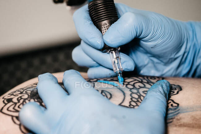 Primo piano colpo di mani in guanti di lattice utilizzando la macchina per colorare il tatuaggio con inchiostro blu in studio — Foto stock