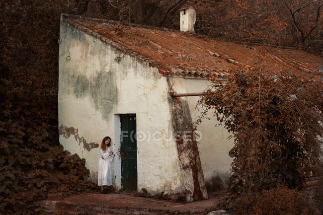 Молода жінка в білій сукні спирається на стіну — стокове фото