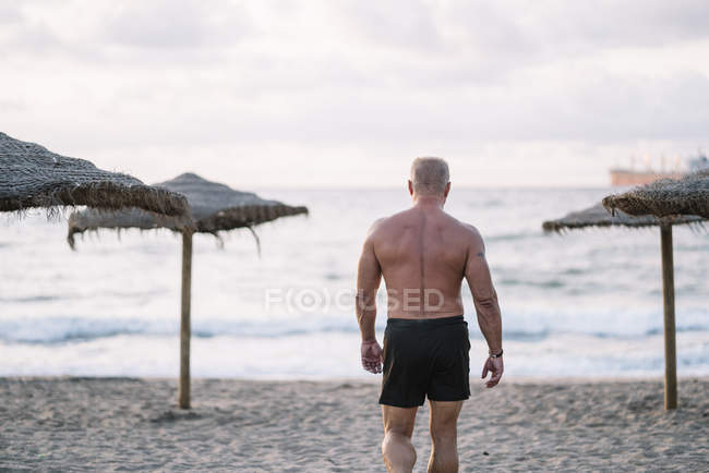 Forte vecchio che cammina sulla spiaggia — Foto stock