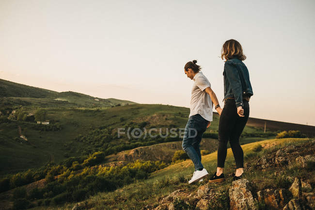 Side view of young man and woman walking down stony hill while spending time in nature together — Stock Photo