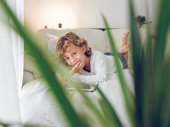 Menino sorrindo usando tablet no sofá em casa — Fotografia de Stock