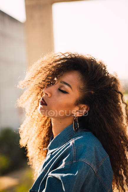Stylish African American young woman in denim shirt with closed eyes in sunlight — Stock Photo