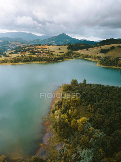 Зеленый лес на голубом озере и небольшая деревня на холме в Pais Vasco, Страна Басков, Испания — стоковое фото