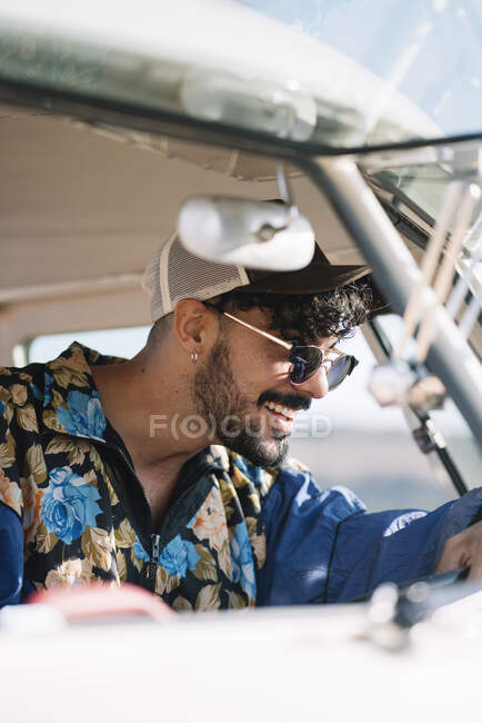 Seitenansicht eines hübschen jungen Mannes in stylischem Outfit, der auf dem Fahrersitz sitzt und auf Reisen Retro-Van lenkt — Stockfoto