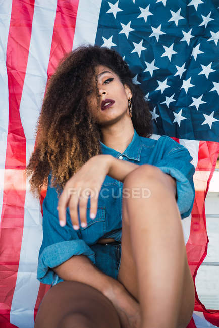 Молодая женщина в джинсовой одежде сидит перед флагом Америки — стоковое фото