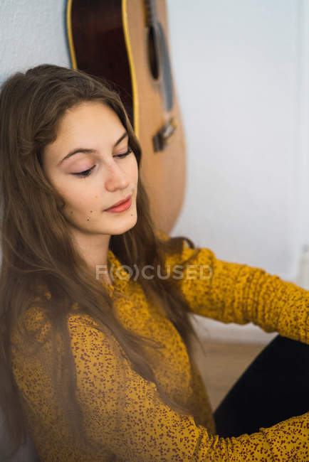 Женщина сидит рядом с гитарой — стоковое фото