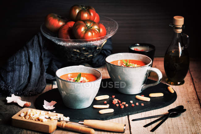 Gazpacho de tomate servido con huevo y jamón en tazas sobre pizarra - foto de stock