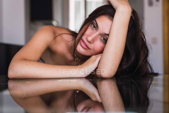 Young sensual woman leaning on glass table with hand in hair — Stock Photo
