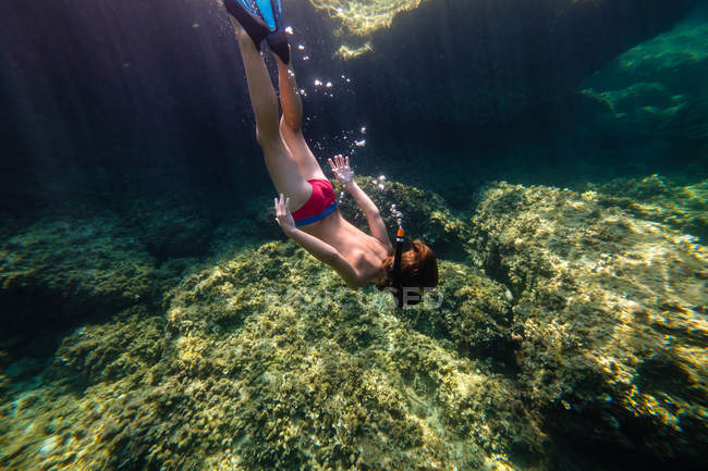 Menino irreconhecível mergulhando no mar em direção a rocha — Fotografia de Stock