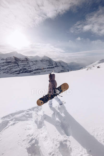 Mulher irreconhecível vestindo roupas quentes e snowboard com munição especial deslizando para baixo? no fundo do céu nublado — Fotografia de Stock