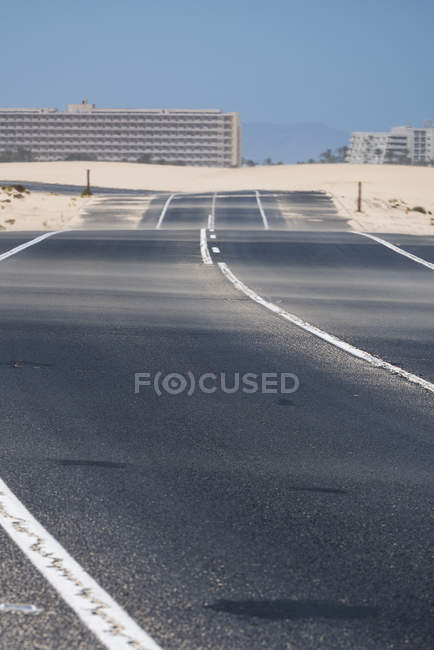 Carretera en el desierto de Fuerteventura con edificios urbanos sobre fondo borroso, Islas Canarias - foto de stock