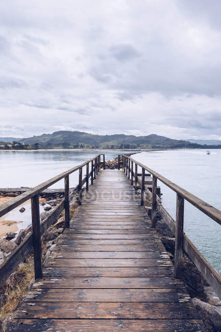Weathered umber pier located on shore near surface of calm water on cloudy day in Asturias, Spain — Stock Photo