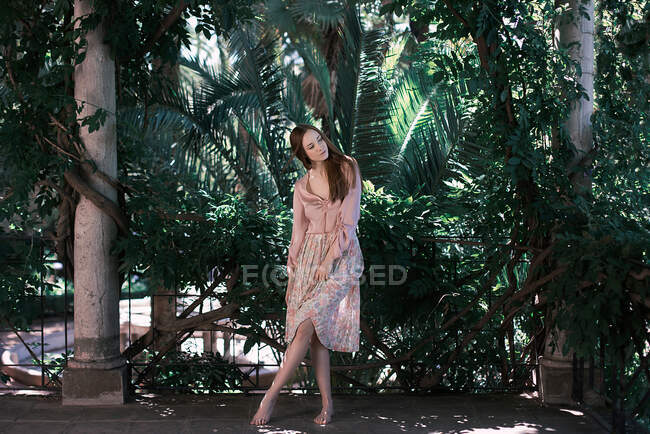 Красива молода жінка в елегантному вбранні танцює, стоячи на тлі чудового зеленого саду — стокове фото