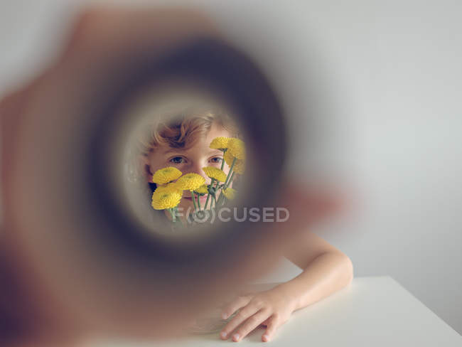 View of lovely boy with bunch of bright dandelions through paper tube on white background — Stock Photo