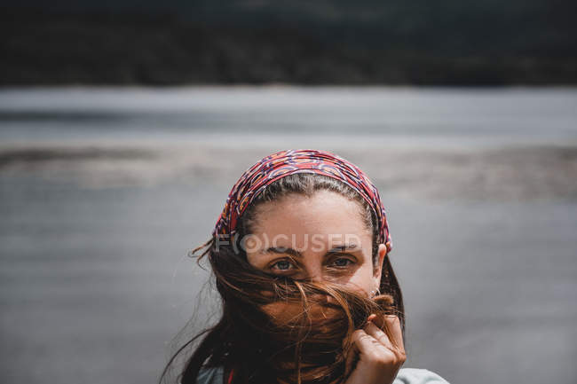 Mujer alegre de pie cerca del río con el pelo soplado por el viento - foto de stock