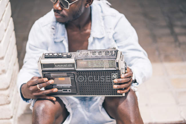 Jeune homme assis avec dispositif de radio vintage et regardant loin — Photo de stock