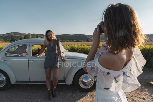 Mujer con estilo tomando fotos a un amigo en el campo con cámara fotográfica - foto de stock